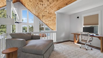 Ein modernes Schlafzimmer im Loftsstil mit schrägverdeckter Decke, einem grauen Sofa, einem Holztisch und einem großen Fenster.