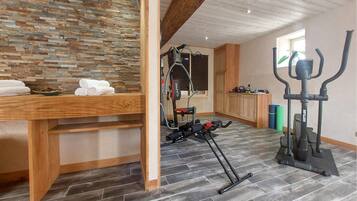 Quarto com parede de pedra, móveis de madeira, equipamentos de ginástica e uma janela.