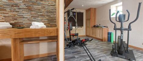 A room with a stone wall, wooden furniture, exercise equipment, and a window.
