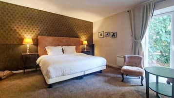 Quarto de hotel com uma cama grande, duas luminárias de cabeceira, uma cadeira, uma mesinha e vista para o verde pela janela.