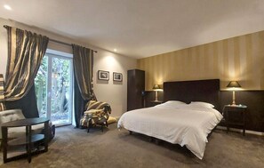 Ein Hotelzimmer mit einem großen Bett, einem Sessel, einem Schreibtisch und Blick ins Freie.