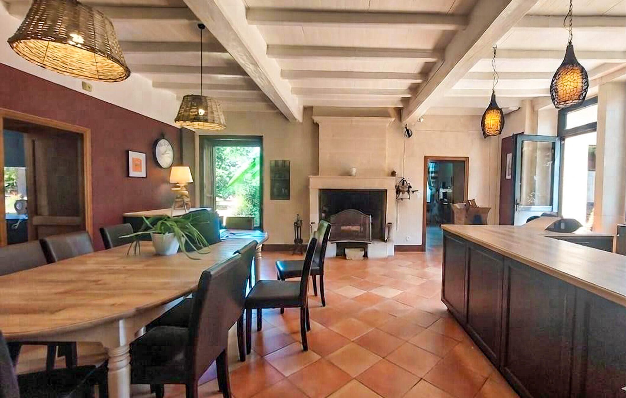 A spacious dining area with a wooden table and chairs, a fireplace, and hanging pendant lights.
