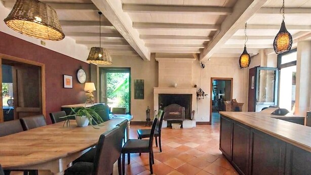 A spacious dining area with a wooden table and chairs, a fireplace, and hanging pendant lights. - Domaine de luxe avec piscine (Meursac)