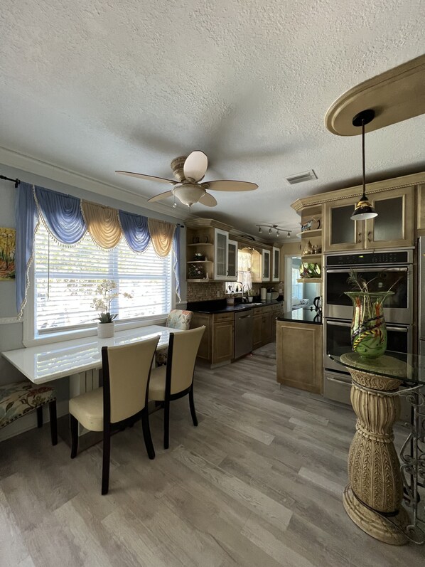 Una cocina con mesa, sillas, ventilador de techo y refrigerador.