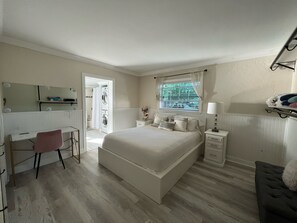 Un dormitorio con cama, escritorio, silla, ventana y mesita de noche.