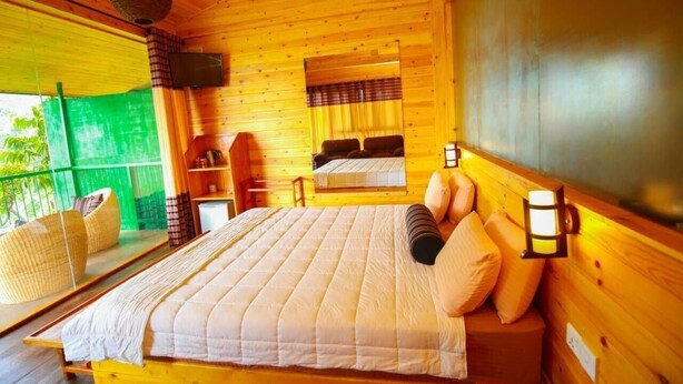 A wooden cabin room with a bed, a chair, a small table, and a television. - Ella Taxi (Ella)