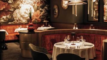 Ein Restaurant mit einem runden Tisch für zwei Personen, einer rot gepolsterten Bank und einem dekorativen Kronleuchter.