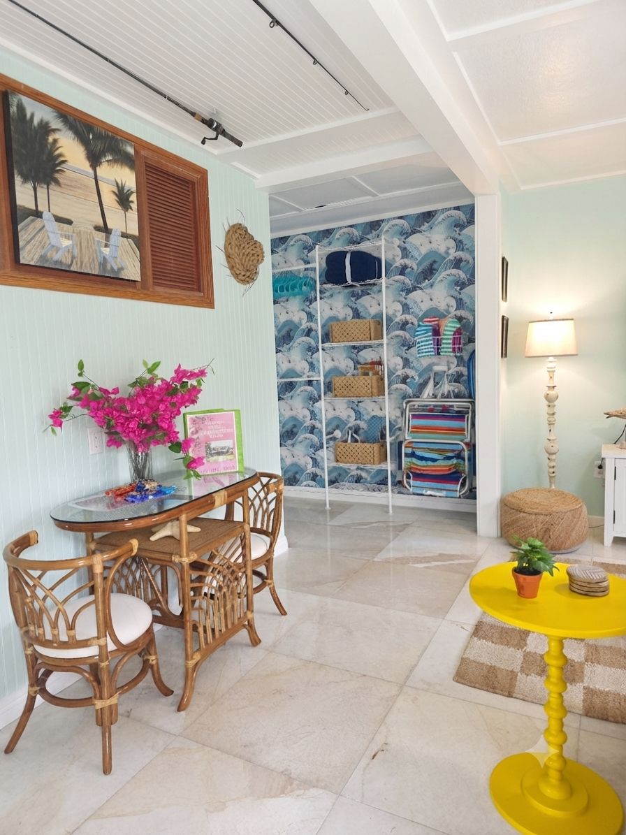 A room with a dining table, chairs, a yellow stool, a lamp, and a wall with a blue and white pattern.
