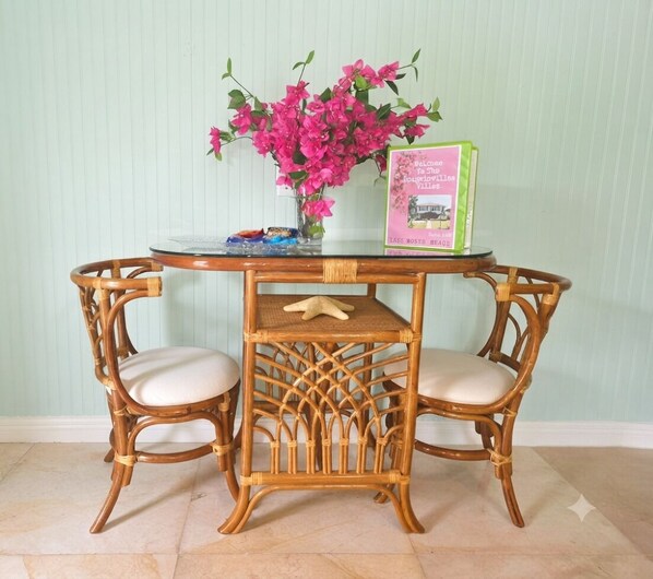 A round table with two wicker chairs, a vase of pink flowers, and a welcome sign. - Bougainvillea Villa #3. 2 blocks to downtown LWB and 1 mile to beach
 PETS OK! (Lake Worth Beach)
