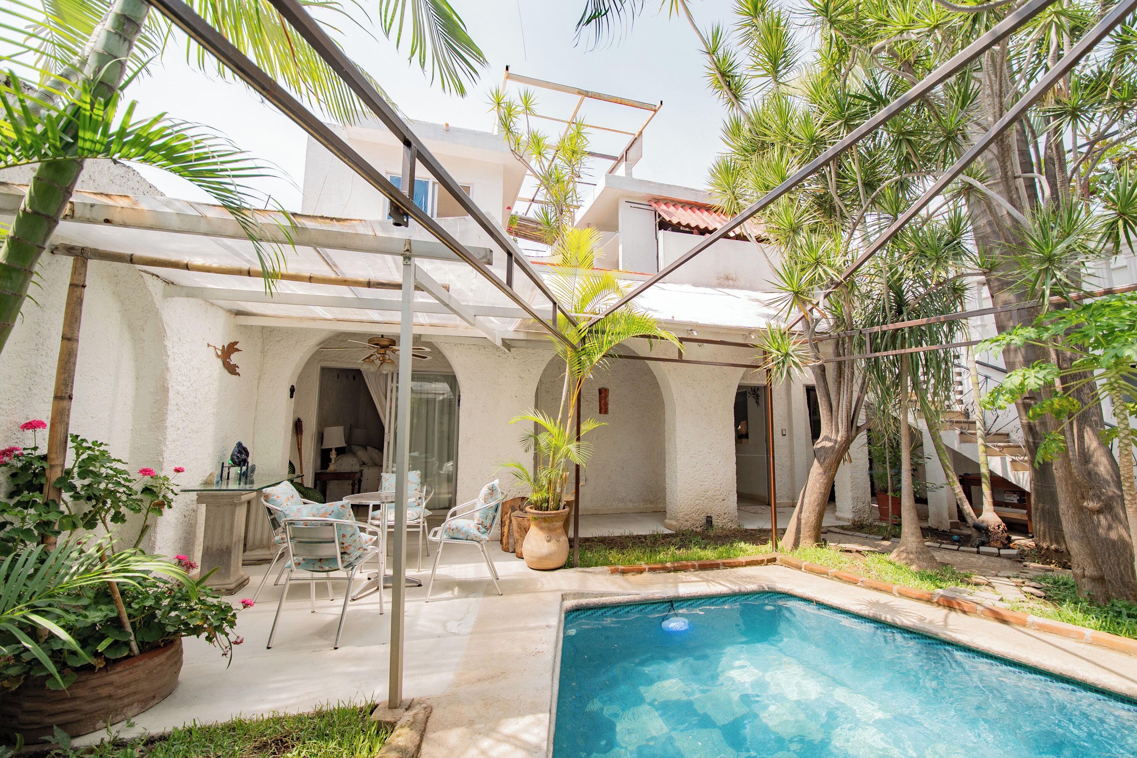A pool area with a clear blue pool, surrounded by potted plants and a seating area with chairs.