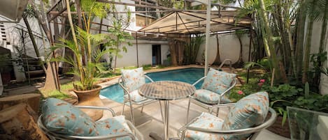 A covered outdoor area with a pool, chairs, and potted plants.