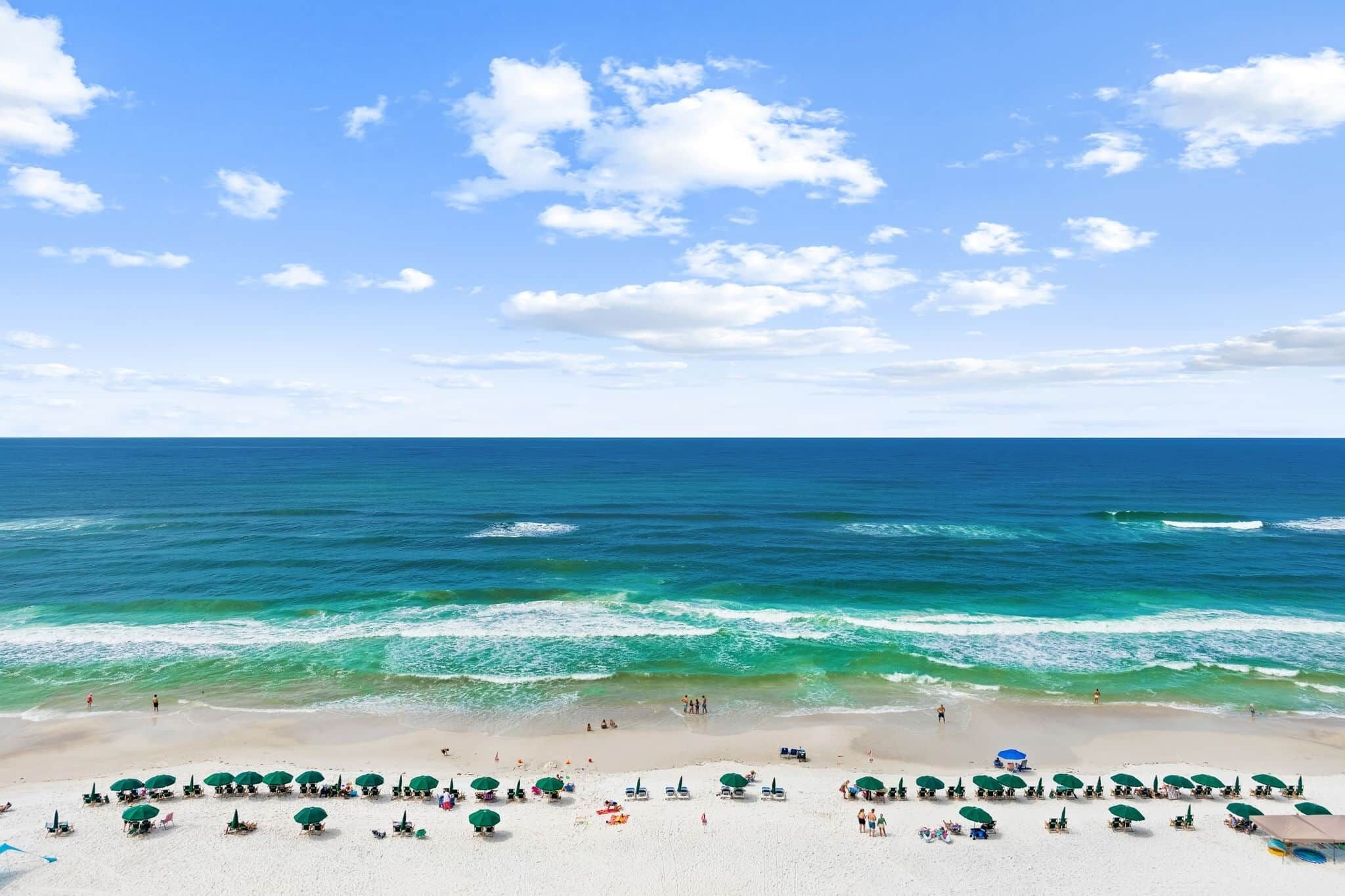 A beach with rows of umbrellas and lounge chairs, a clear sky, and the ocean.