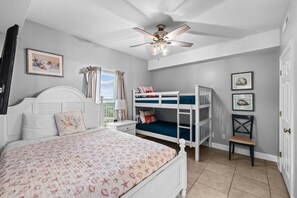 Ein Schlafzimmer mit Etagenbett, einem Einzelbett, einem Deckenventilator und einem Fenster mit Vorhängen.