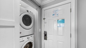 Una sala de bugaderia amb dues rentadores frontals apilades i una porta blanca amb cartells informatius.