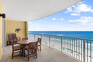 A balcony with a table and chairs, a view of the beach, and a dolphin sculpture. - Emerald Isle: Beachfront Condo, Pool, Balcony (Panama City Beach)