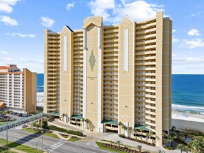 A high-rise hotel with multiple balconies, a beach view, and a parking area.