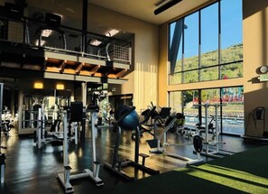 Un gimnasio con equipo de ejercicio variado, amplias ventanas y un entrepiso.