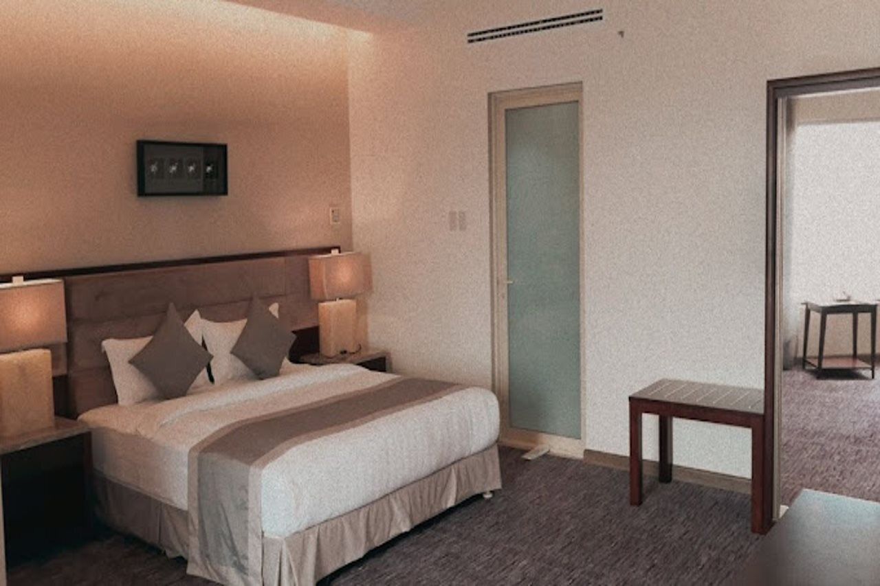 Een hotelkamer met een bed, nachtlampjes, een klein tafeltje en een deur.