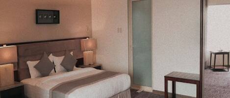 Een hotelkamer met een bed, nachtlampjes, een klein tafeltje en een deur.