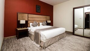 Ein Hotelzimmer mit einem großen Bett, einem Holz-Kopfteil, zwei Nachttischen mit Lampen, einer roten Akzentwand und einem großen Spiegel.
