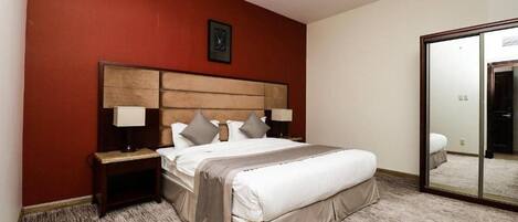 A hotel room with a large bed, a wooden headboard, two bedside tables with lamps, a red accent wall, and a large mirror.