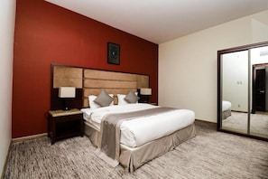 Habitación de hotel con una cama grande, cabecera de madera, dos mesitas de noche con lámparas, una pared de acento roja y un espejo amplio.