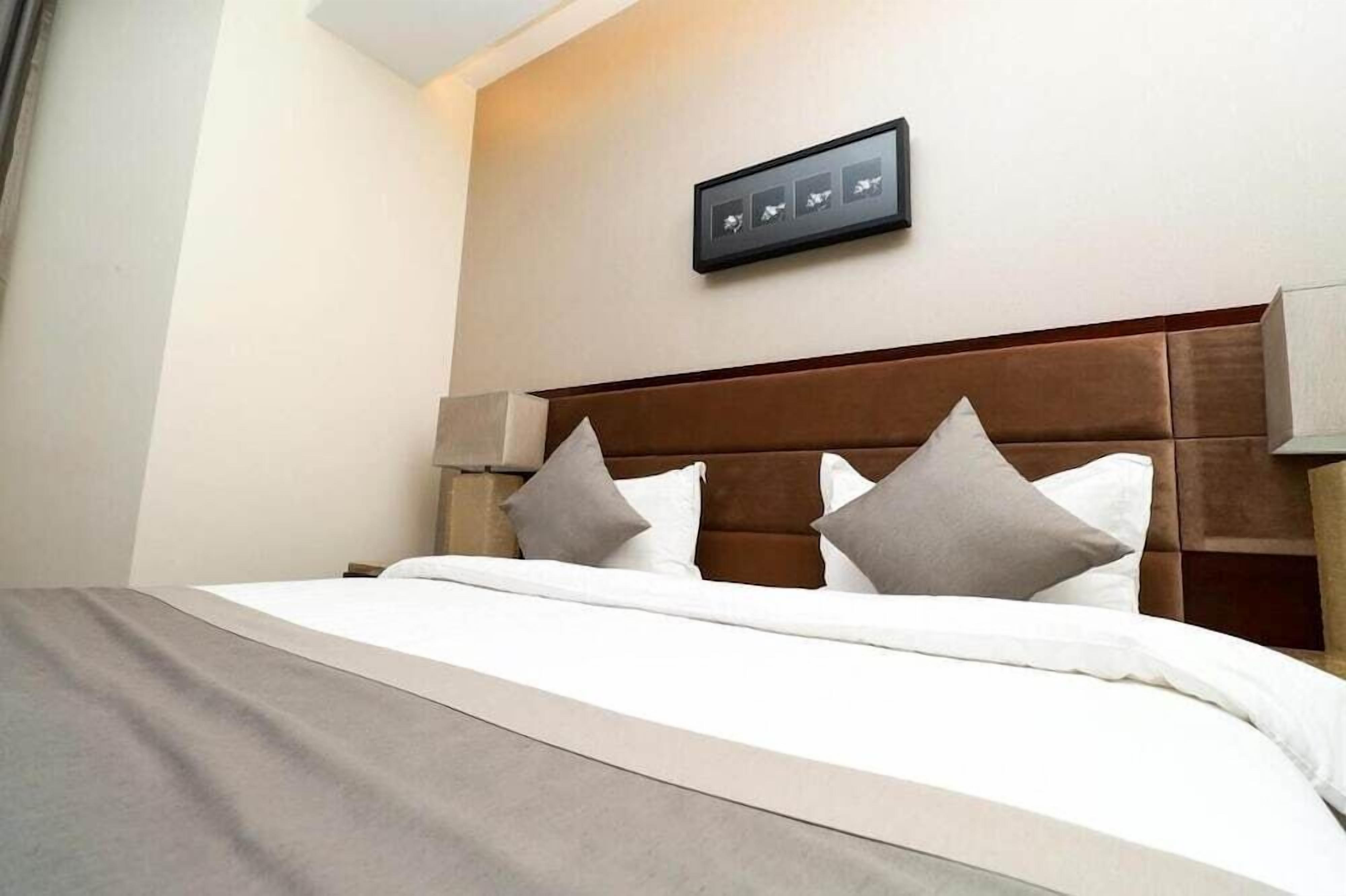 A hotel room with a bed, a headboard, and a wall-mounted picture.