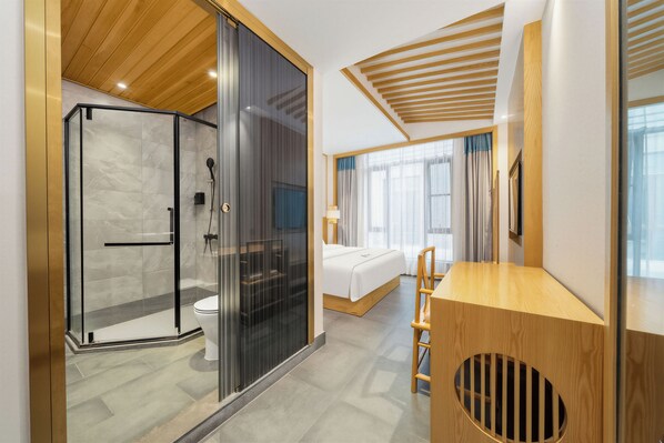 A modern hotel room with a glass-enclosed shower, a wooden ceiling, a bed with a white mattress, and a wooden desk.