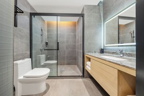 Un baño moderno con ducha de vidrio, inodoro y tocador con lavamanos y espejo.