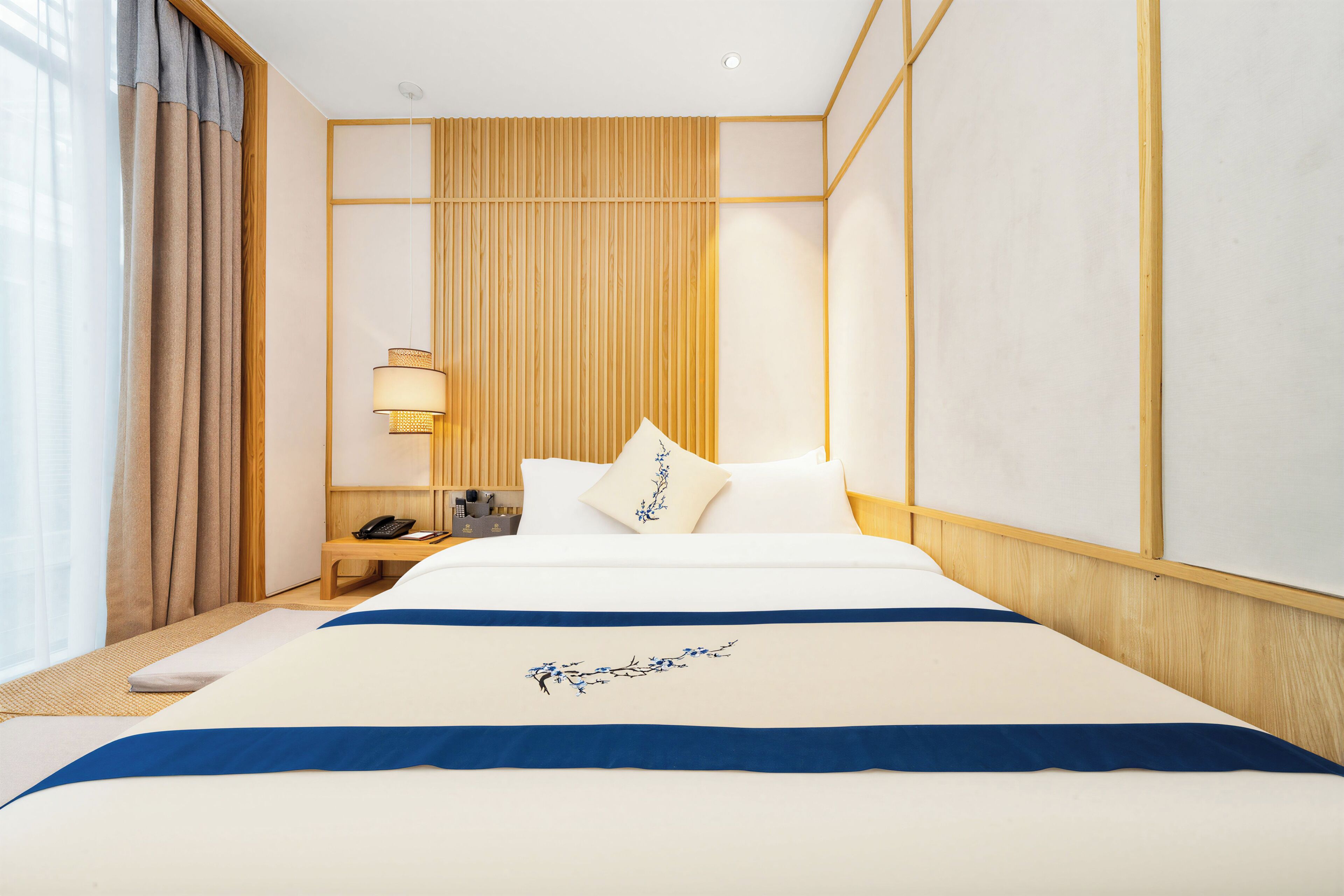 Habitación de hotel con una cama grande, una mesita de noche con lámpara y vistas al exterior por la ventana.