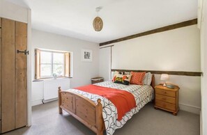 A bedroom with a wooden bed, a bedside table with a lamp, a window with a view, and a radiator. - 17th Century Farmhouse - Near Silverstone Circuit (Towcester)