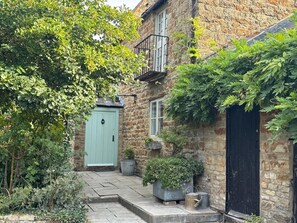 A stone building with a green door, a small balcony, and a garden area with potted plants. - 17th Century Farmhouse - Near Silverstone Circuit (Towcester)