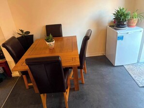 A dining area with a wooden table, black chairs, and a refrigerator with plants on top.