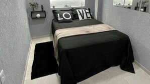 Een moderne slaapkamer met een bed, nachtkastje, spiegel en decoratieve muurkunst.