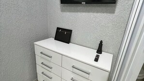 Een badkamer met een witte wastafel, een tv aan de muur en een zwarte fles op het aanrecht.