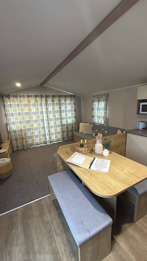 A modern living room with a sofa, a coffee table with decorative items, and a dining area with a bench. - Billing Aquadrome Holiday Park - 2 Bedroom, Silver (Northampton)