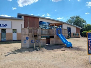 A playground with a slide and climbing area, a building with a sign, and a clear sky. - Billing Aquadrome Holiday Park - 2 Bedroom, Silver (Northampton)