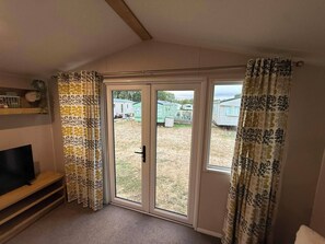 Ein Zimmer mit Fernseher auf einer Ablage, einer Schiebetür zu einem Außenbereich und gemusterten Vorhängen.
