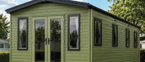 A green mobile home with a front porch and sliding doors.