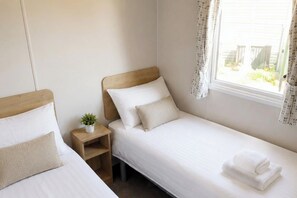 A single-bed room with a wooden headboard, a bedside table with a plant, and a window with curtains. - Billing Aquadrome Holiday Park - 2 Bedroom, Silver (Northampton)