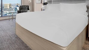 Ein Hotelzimmer mit einem großen Bett, einem Sessel, einem Schreibtisch und Blick auf die Stadt.
