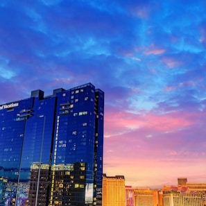 A high-rise hotel with a modern glass facade and illuminated windows, set against a colorful sky at dusk.