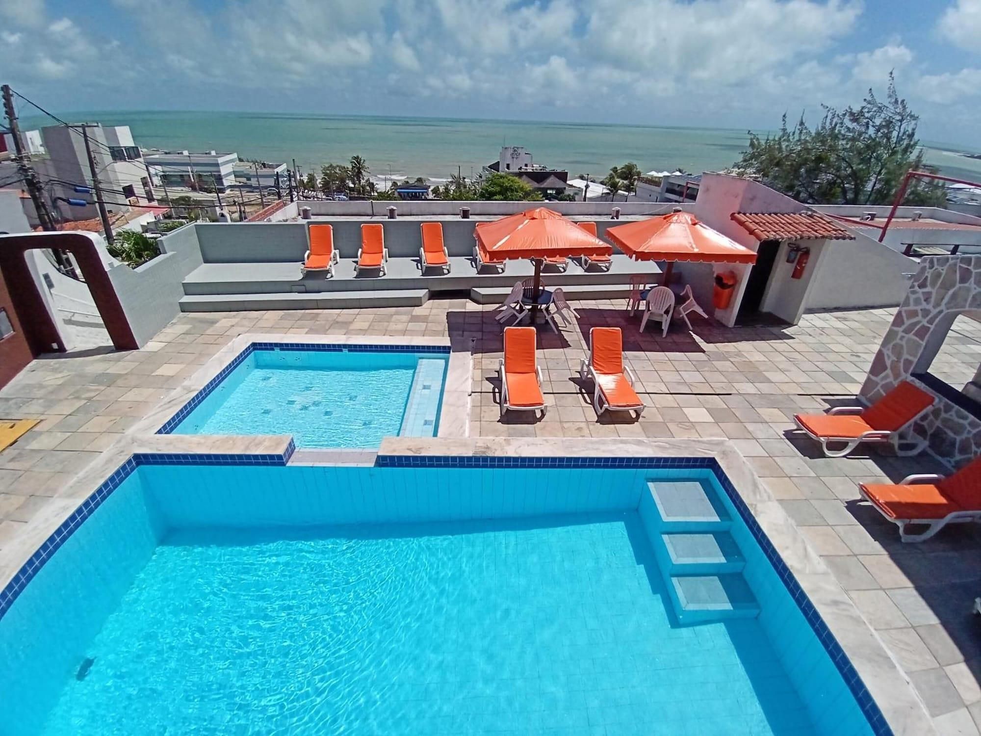 A rooftop pool area with two pools, lounge chairs, and umbrellas.