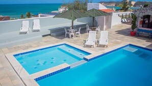 Ein Poolbereich mit Liegestühlen, einer Bar und Blick aufs Meer.