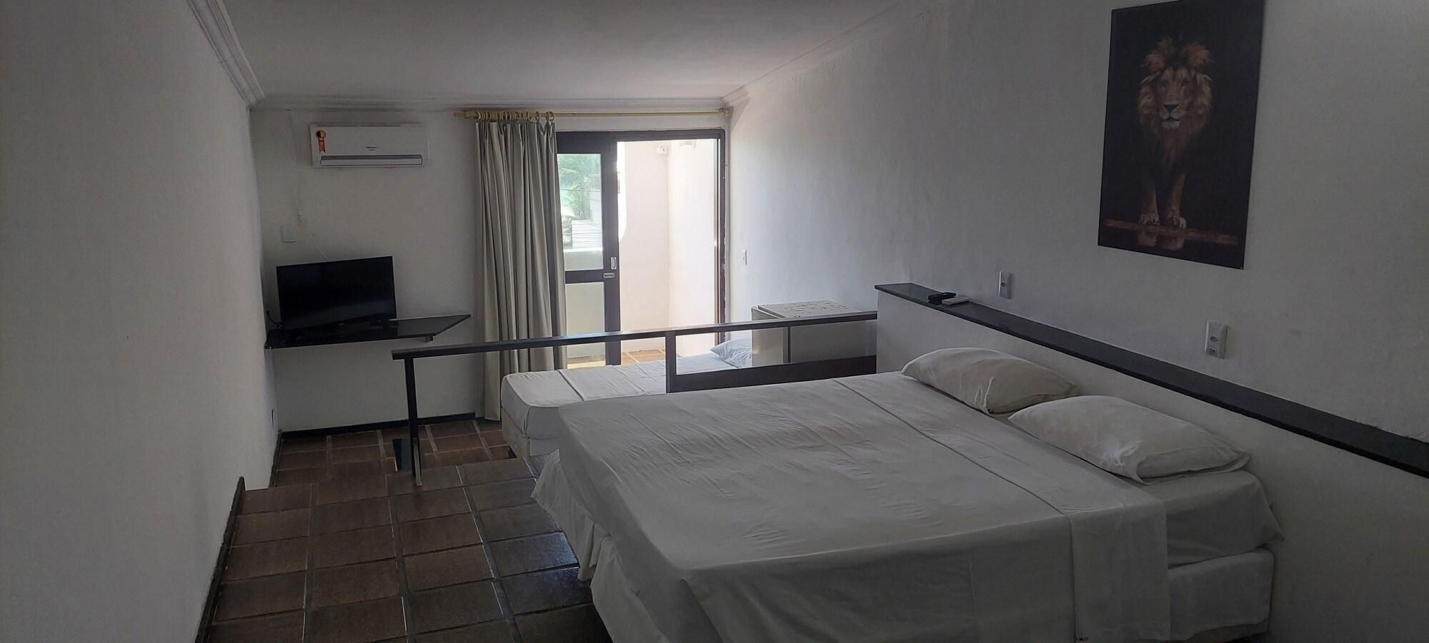 Habitación de hotel con cama, escritorio, televisor y ventana con cortinas.