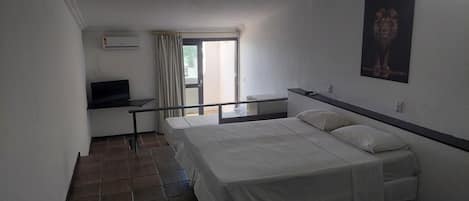 Habitación de hotel con cama, escritorio, televisor y ventana con cortinas.