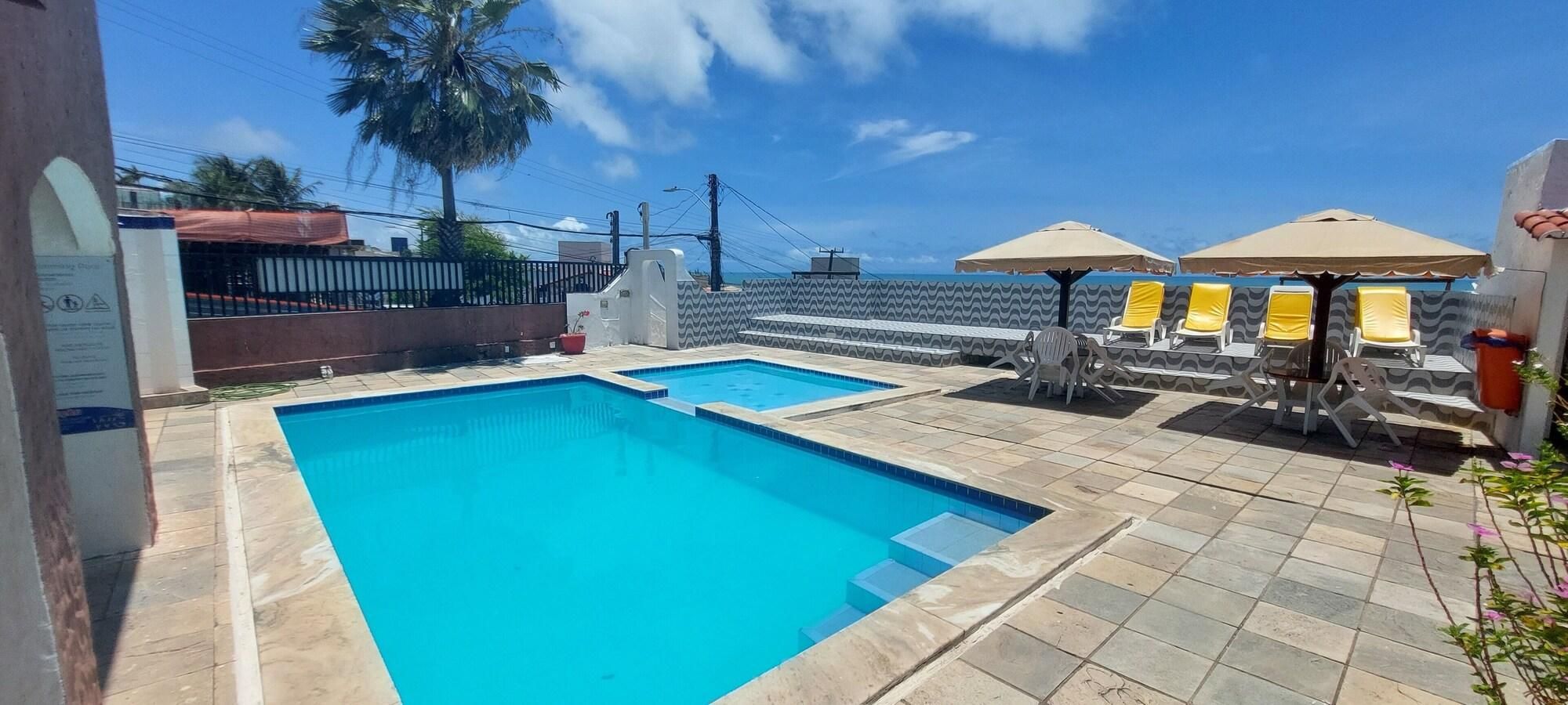 A swimming pool with a tiled deck, lounge chairs, and umbrellas.