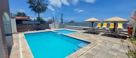 A swimming pool with a tiled deck, lounge chairs, and umbrellas.