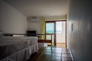 A bedroom with a bed, a desk, and a view of the sea through a door. - Sol Praia Ponta Negra (Natal)