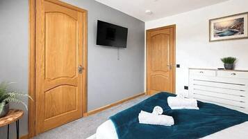 A hotel room with a bed, a television mounted on the wall, a wooden door, and a dresser with a plant on it.